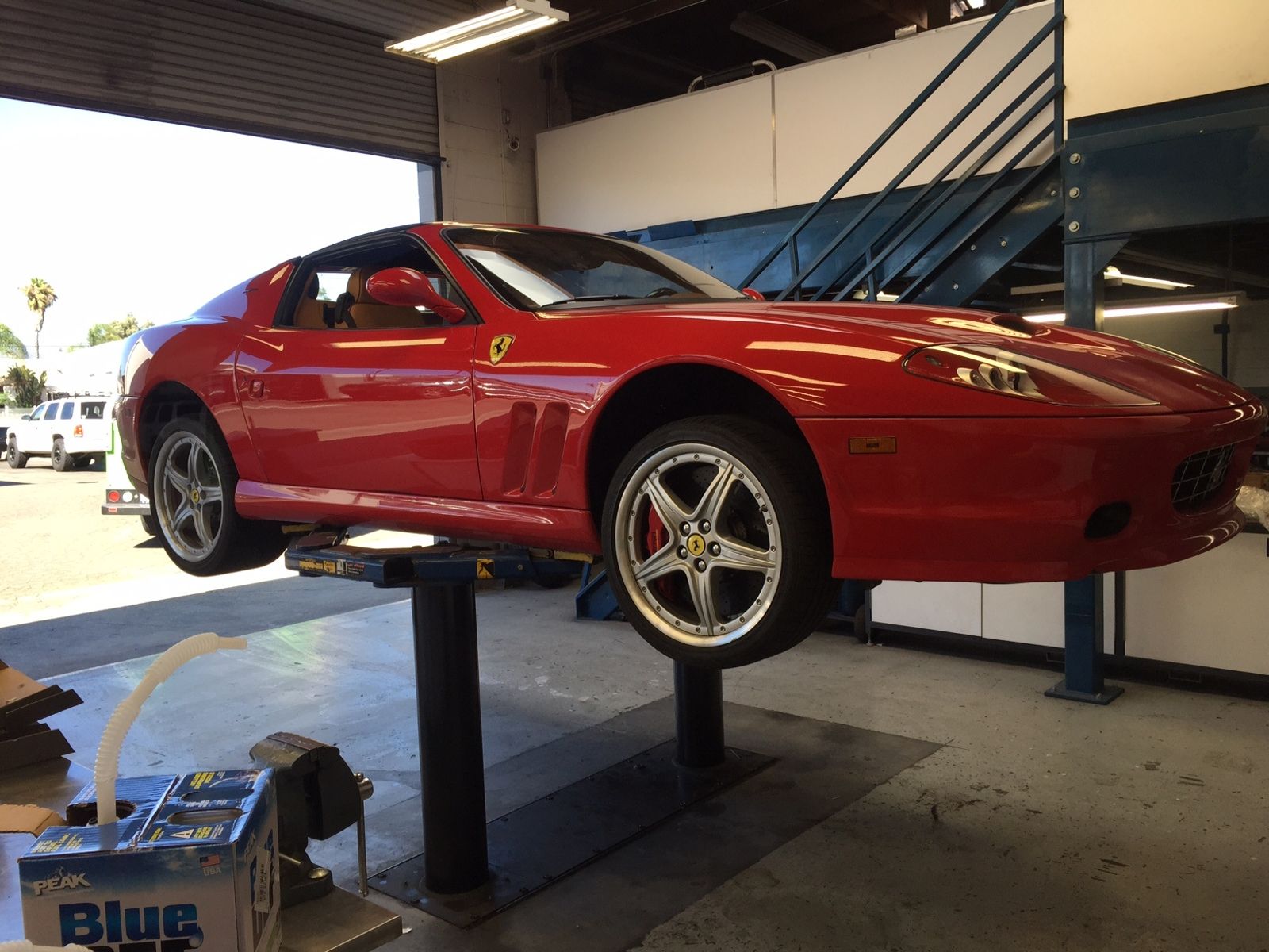 Red Ferrari sports car raised on a two-post lift in the service bay